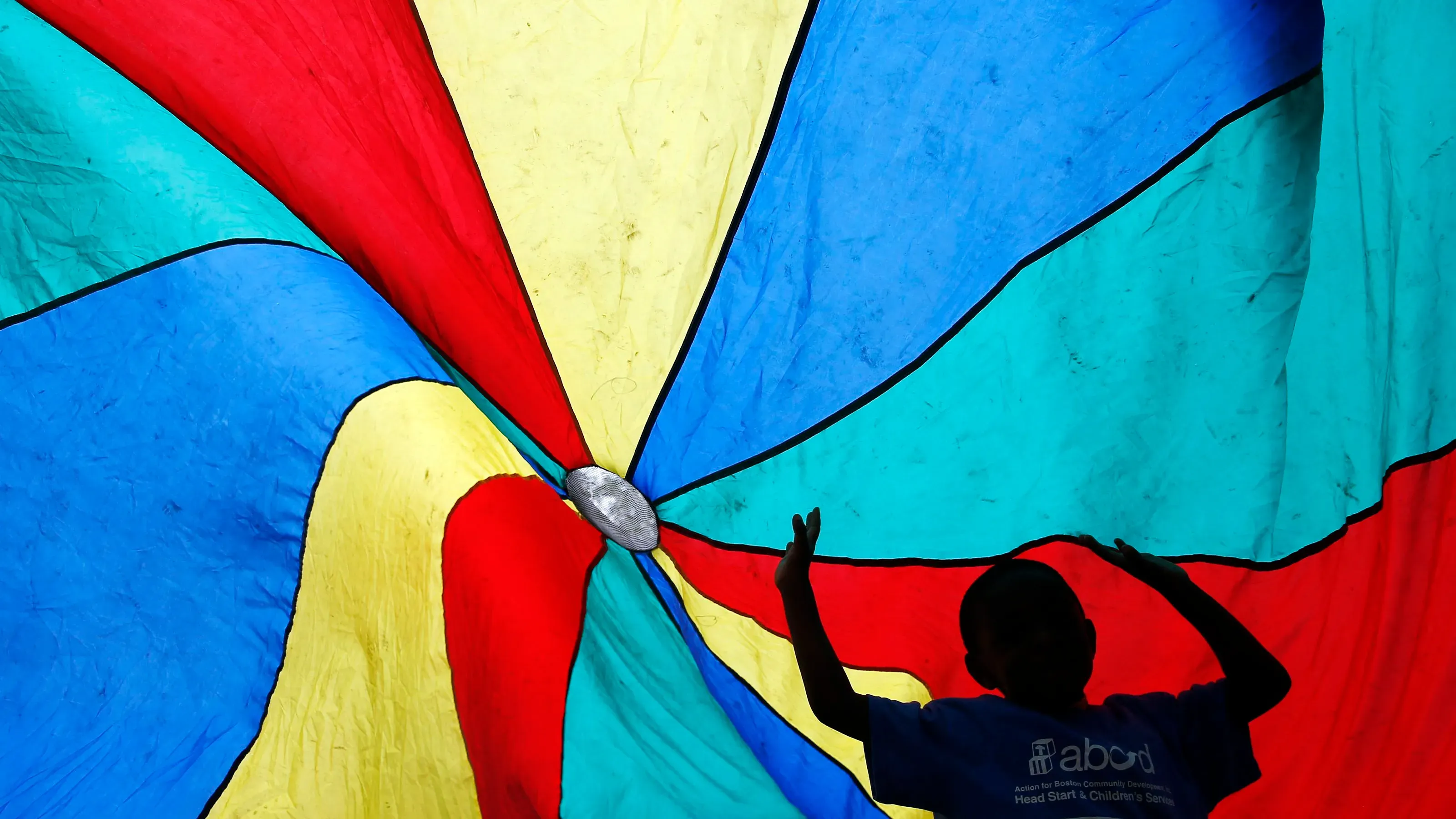 طفل يلعب تحت قماش ملون كبير، يرمز إلى برنامج Head Start الذي يدعم التعليم المبكر للأطفال ذوي الدخل المنخفض.