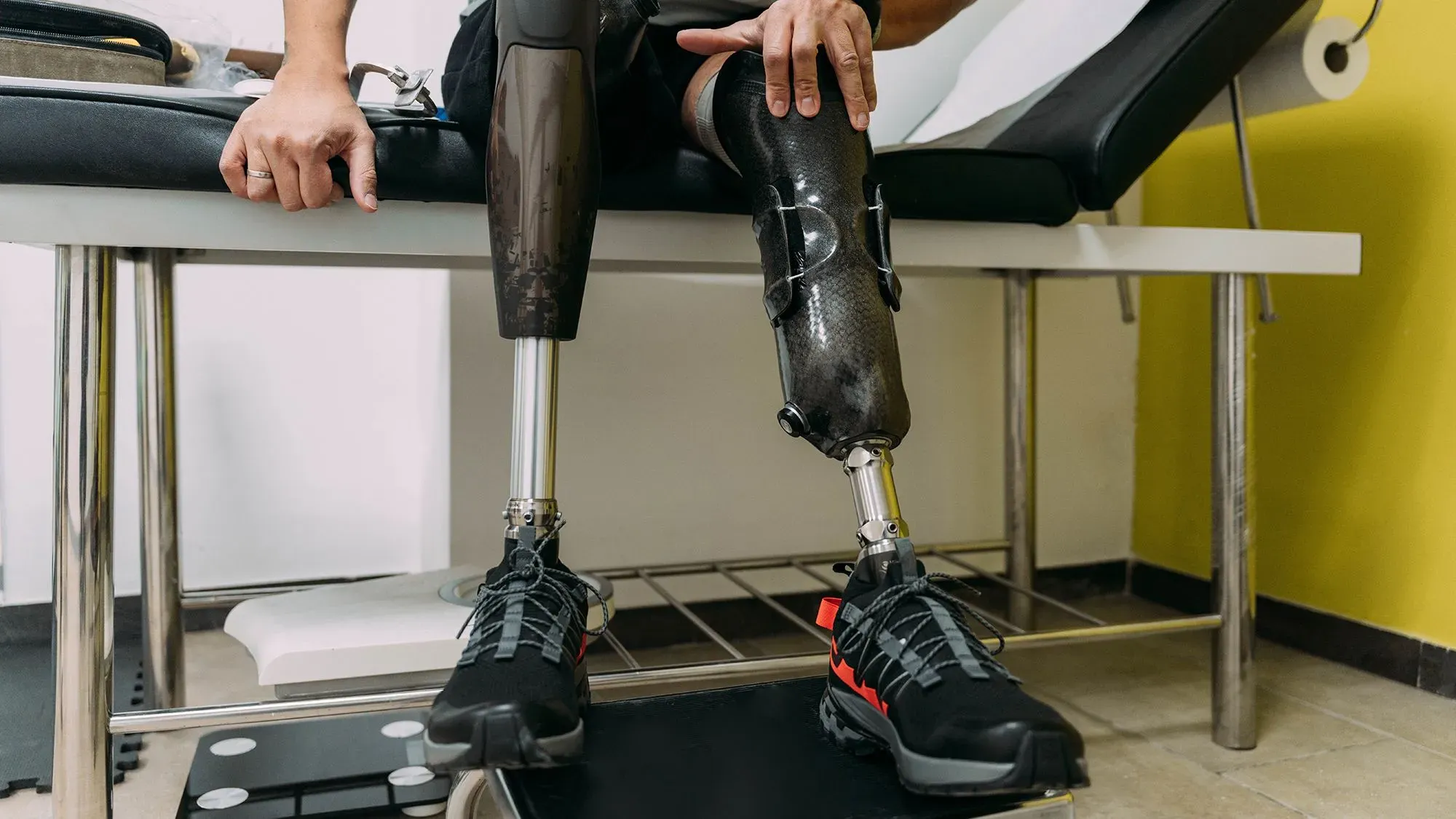 رجل يجلس على أريكة، يظهر ساقاه الاصطناعيان، أحدهما مصنوع من الكربون والآخر معدني، يرتدي حذاء رياضي.