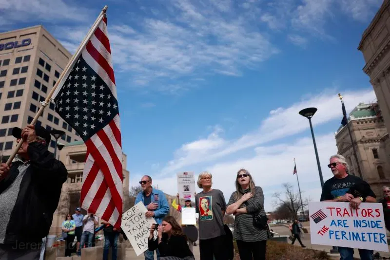 محتجون يحملون لافتات في تظاهرة، مع العلم الأمريكي في المقدمة، تعبيرًا عن القلق بشأن تسريح موظفي وزارة شؤون المحاربين القدامى.