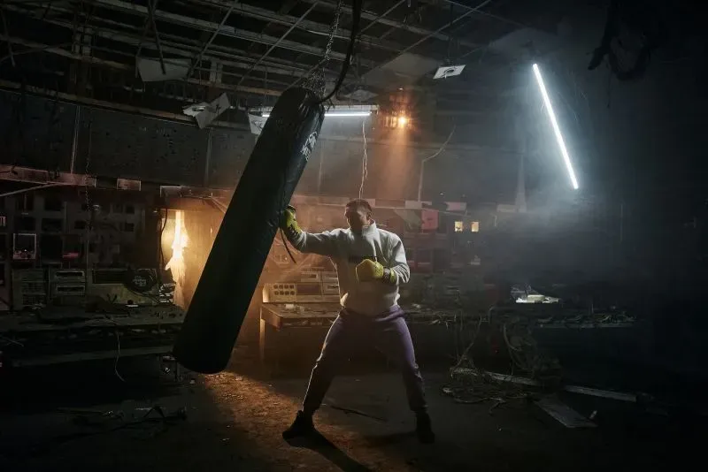 أوليكساندر أوسيك يتدرب على كيس الملاكمة في قاعة رياضية مدمرة، مع أضواء خافتة تعكس أجواء الحرب في أوكرانيا.