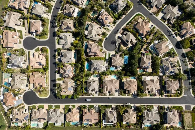 صورة جوية لحي سكني يضم منازل حديثة مع حدائق ومسابح، تعكس تأثير سوق الرهن العقاري الأمريكي.