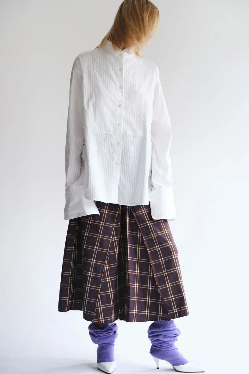 تصميم مبتكر من علامة تاليا ليبكين-كونور، يظهر قميص أبيض مع تنورة مربعة وقطع ملابس ملونة، يعكس تأثيرات الموضة البريطانية الحديثة.