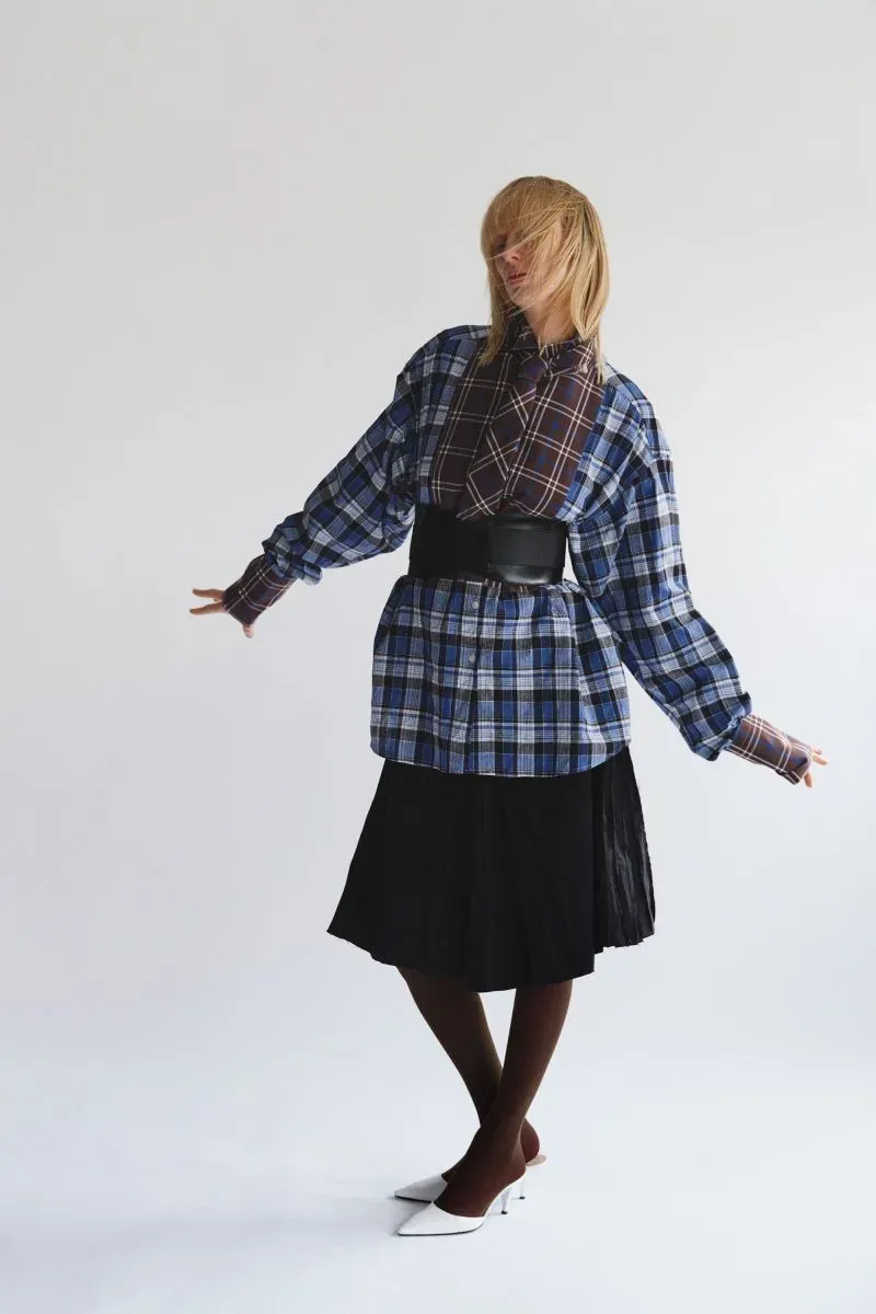 امرأة ترتدي قميصًا مزخرفًا وتنورة سوداء، تعبر عن أسلوبها الفريد في تصميم الأزياء، تعكس تحديات صناعة الموضة البريطانية.