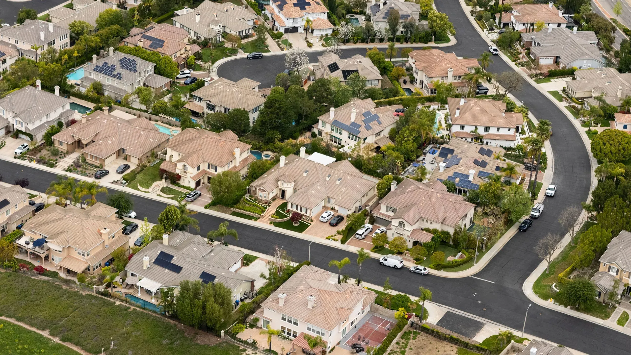 تظهر الصورة منظرًا جويًا لمجمع سكني يتضمن منازل ذات أسطح مائلة، وبعضها مزود بألواح شمسية، في حي هادئ.