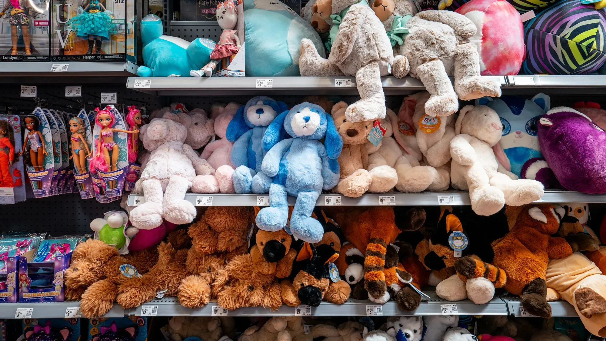 رفوف تحتوي على مجموعة متنوعة من الألعاب المحشوة، بما في ذلك الدمى والدببة، تعرض في متجر وول مارت. تعكس الصورة تأثير التعريفات الجمركية على الأسعار.
