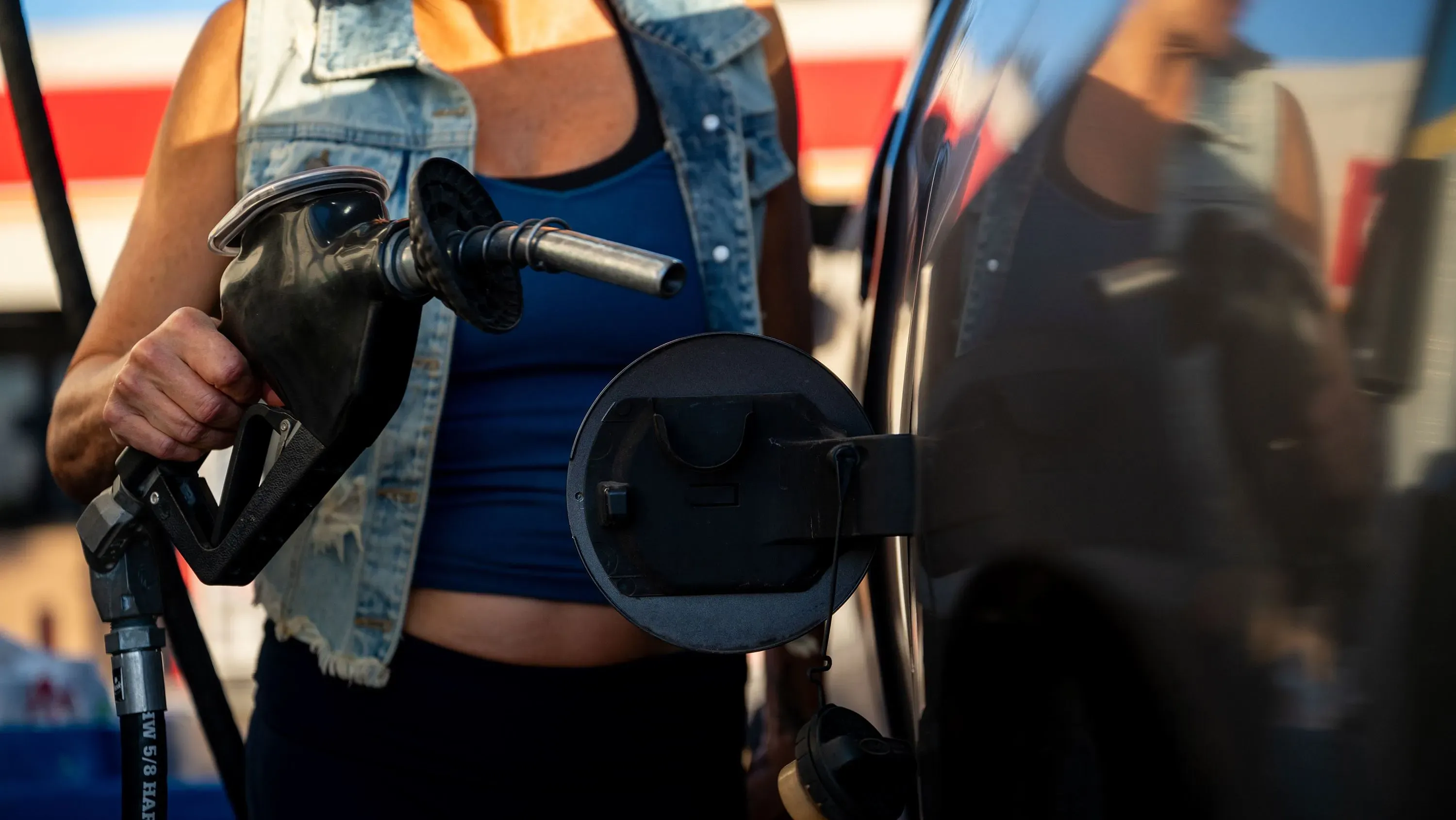 امرأة تمسك بمضخة وقود أثناء تعبئة سيارتها بالبنزين، تعكس أسعار الوقود المستقرة في عطلة يوم الذكرى.