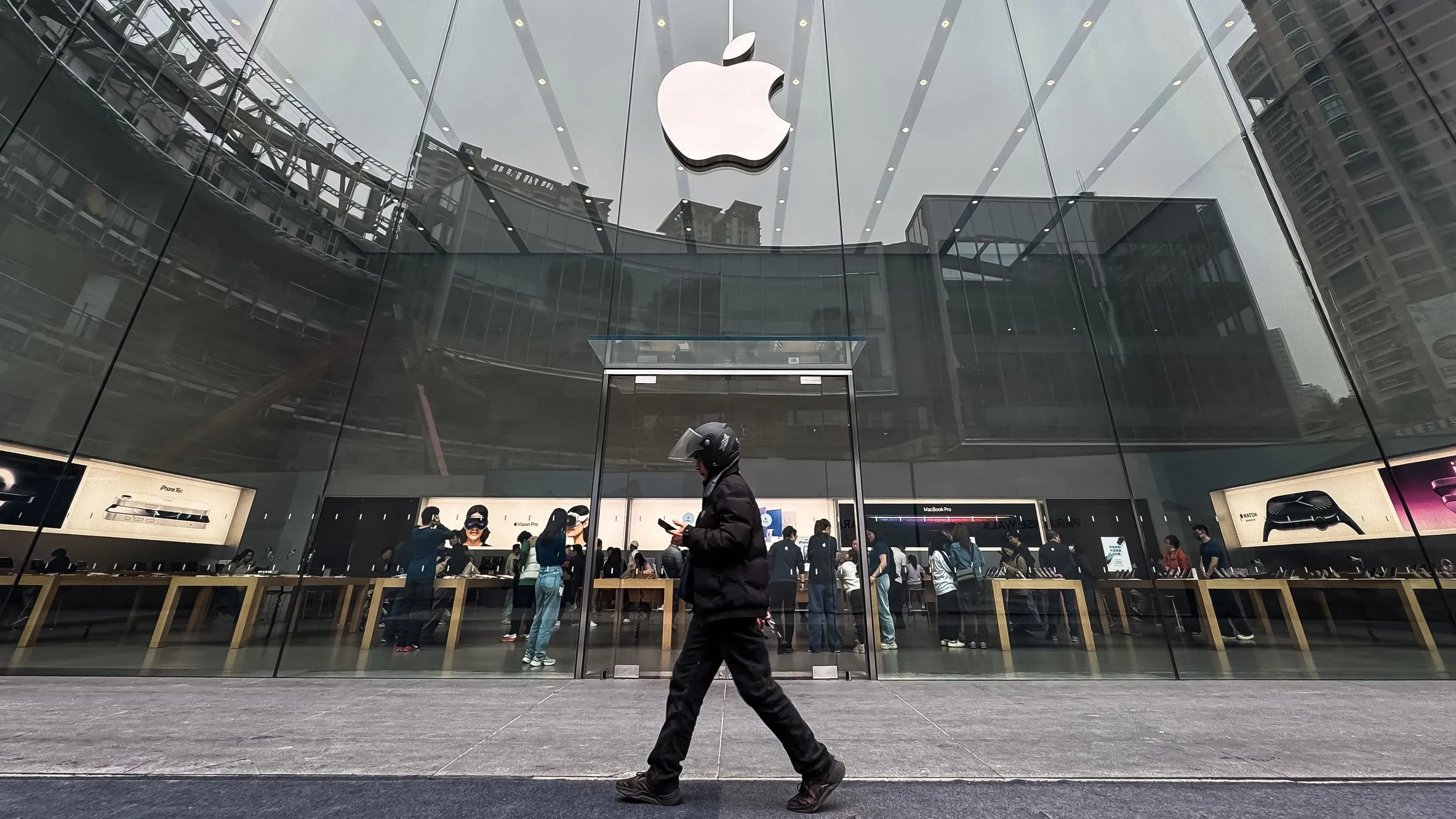 واجهة متجر آبل مع شعار الشركة، حيث يظهر زبائن يتصفحون المنتجات داخل المتجر، وسط توقعات بارتفاع أسعار الآيفون بسبب التعريفات الجمركية.