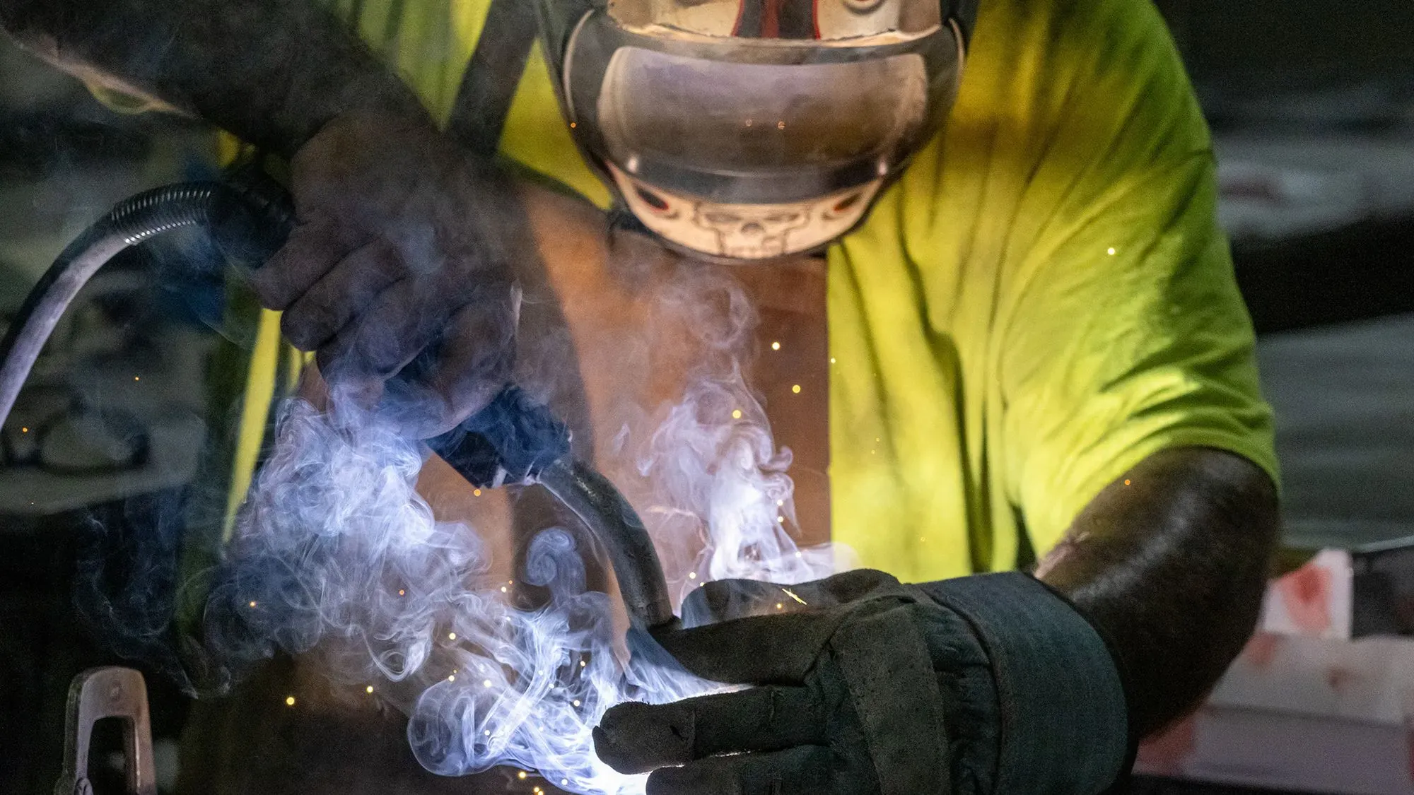 عامل يقوم باللحام في ورشة، مع ظهور دخان وشرر، مما يعكس التغييرات المحتملة في قانون الضرائب الأمريكي وتأثيرها على الصناعات.