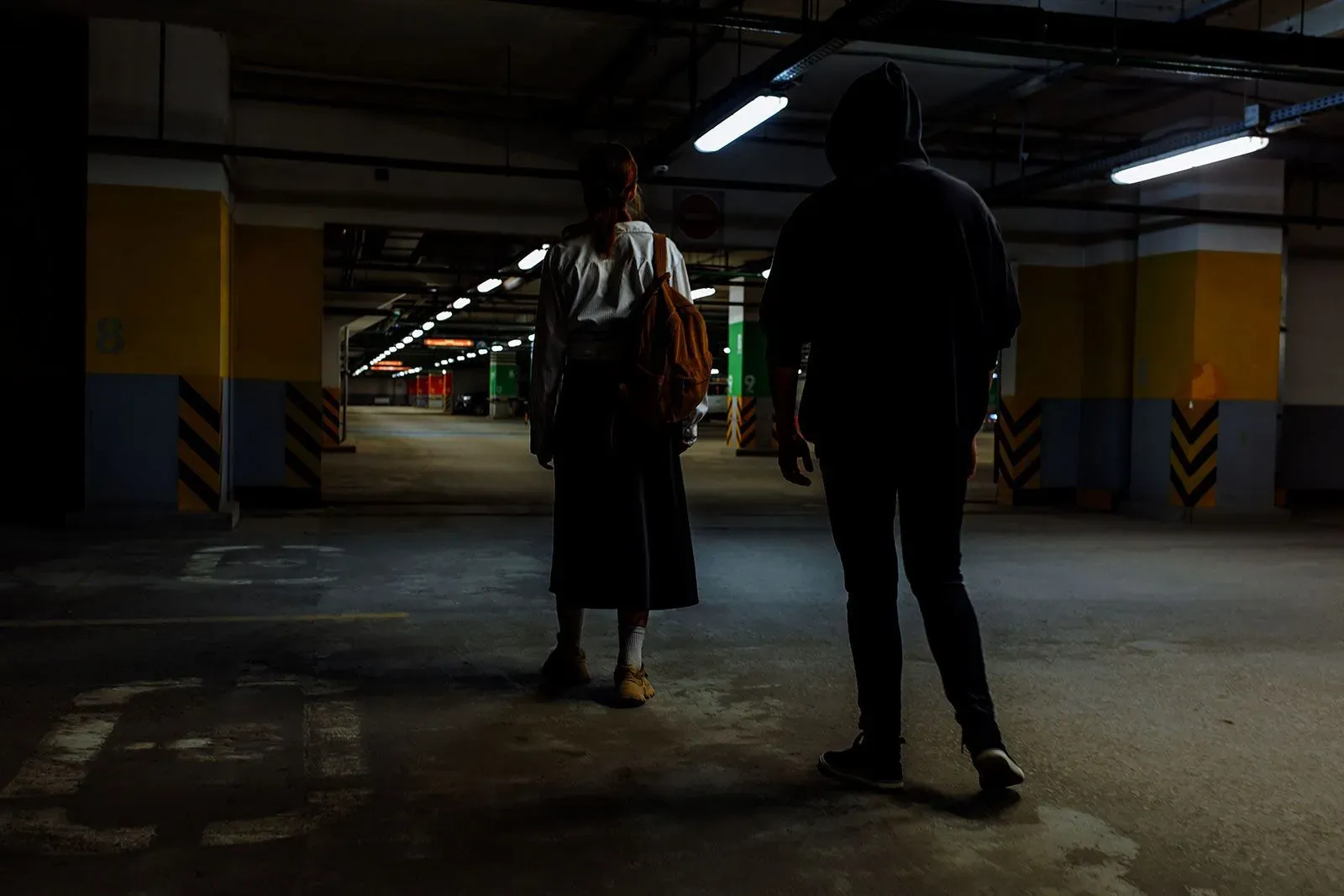 تظهر الصورة شخصين في موقف سيارات مظلم، حيث يقف أحدهما بالقرب من الآخر، مما يعكس مخاطر المواعدة عبر الإنترنت على المراهقين.