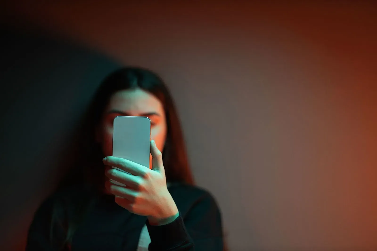 امرأة شابة تحمل هاتفًا ذكيًا أمام وجهها، في إضاءة خافتة، تعكس القلق بشأن المخاطر المحتملة لتطبيقات المواعدة على المراهقين.