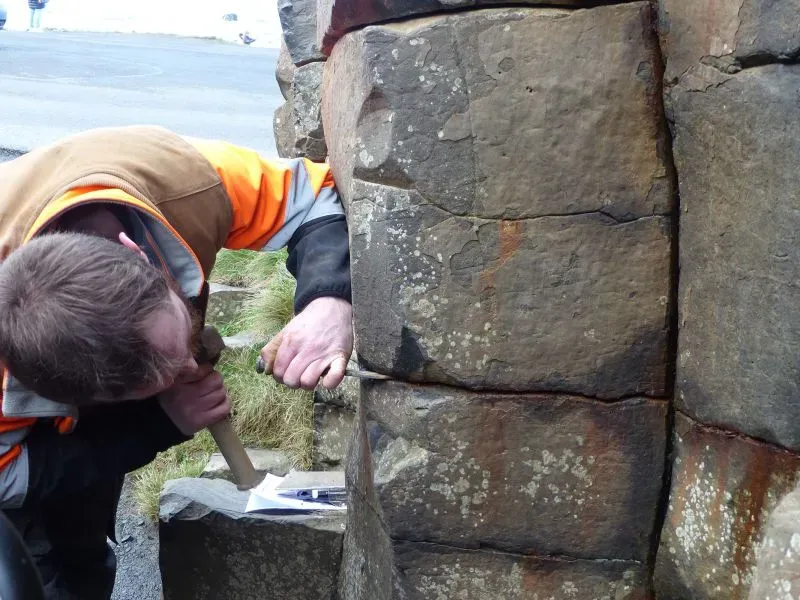 عامل يقوم بإجراء أعمال صيانة على أعمدة جسر العملاق، محذرًا من الأضرار الناتجة عن العملات المعدنية التي تتركها الزوار.