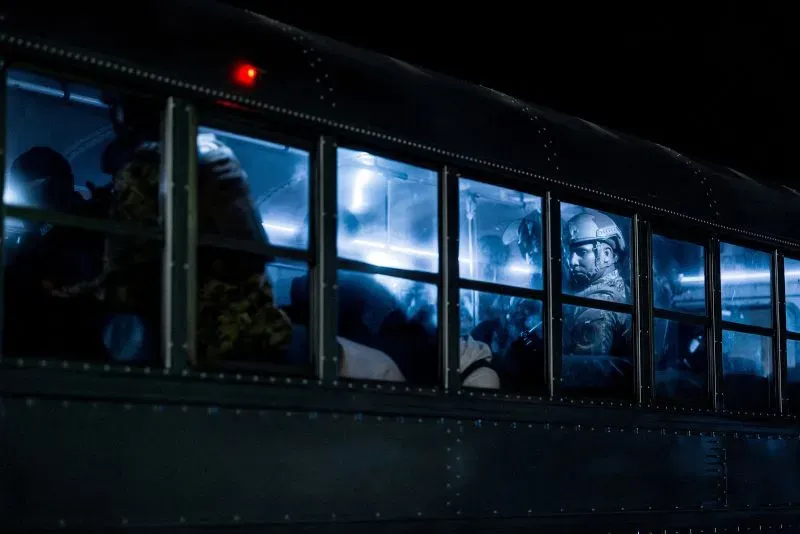 حافلة مظلمة تحمل مهاجرين فنزويليين، مع وجود ضباط أمن بزي رسمي، تعكس حالة الترحيل القسري إلى السلفادور.