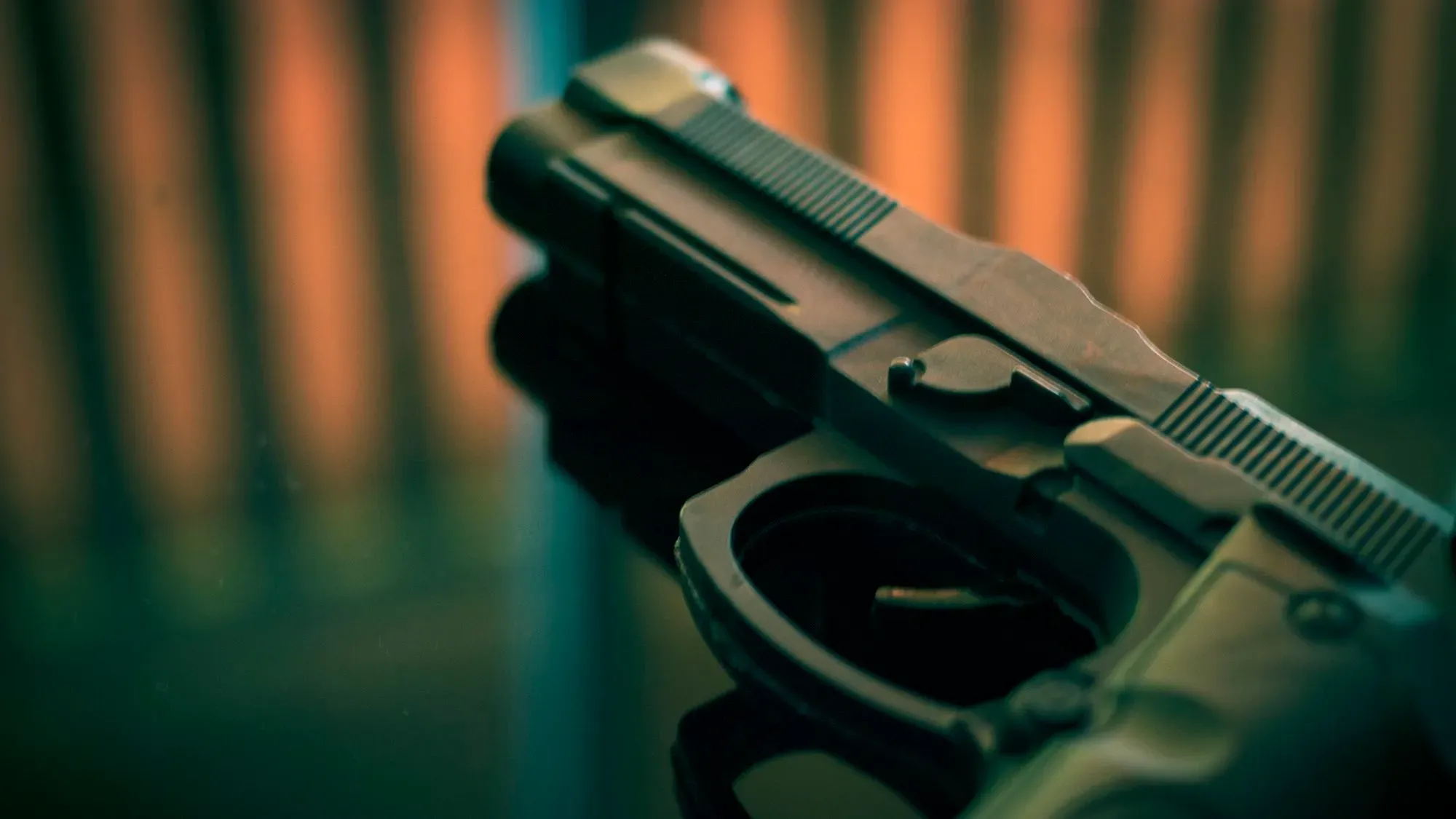 مسدس موضوع على سطح زجاجي، يعكس الضوء، يرمز إلى أزمة العنف المسلح في الولايات المتحدة وتأثيرها على الصحة العامة.