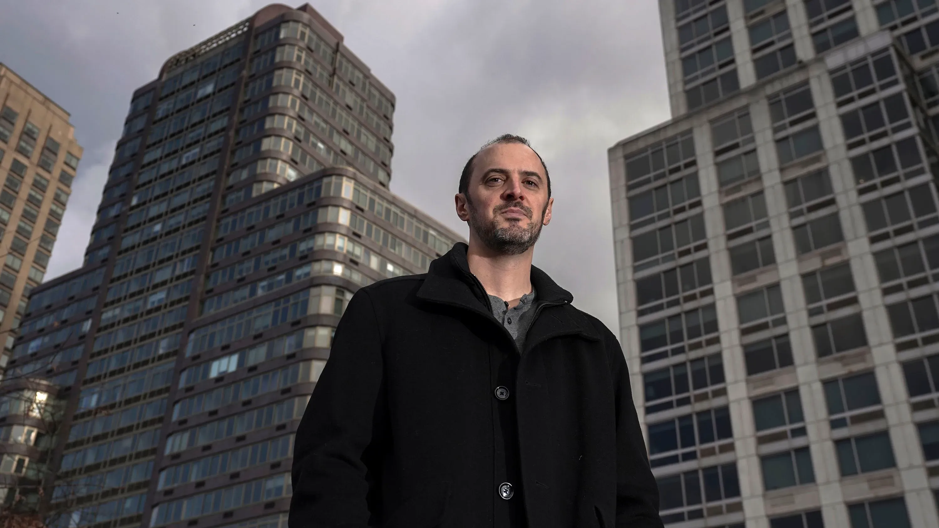 رجل يرتدي معطفًا أسود يقف أمام مباني شاهقة، مع تعبير جاد، معبرًا عن تحديات البيع على المكشوف في وول ستريت.