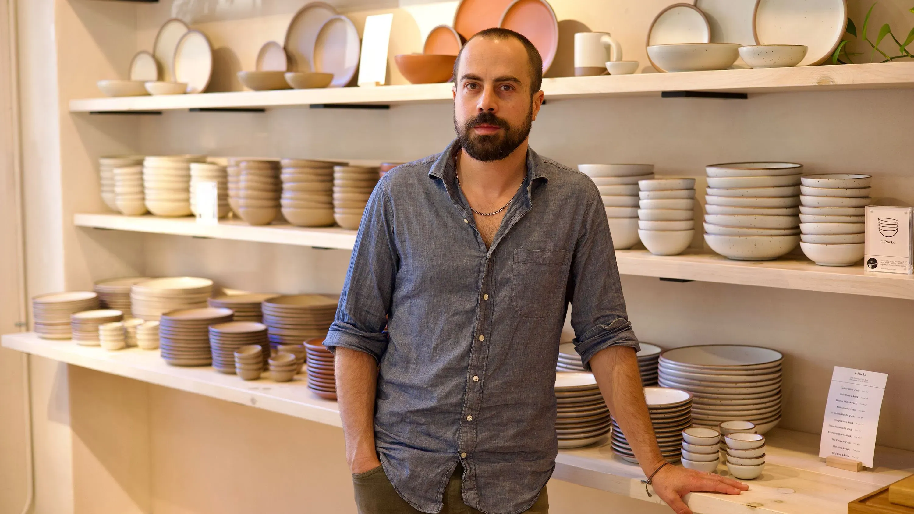 أليكس ماتيس، صانع خزف، يقف أمام رف مليء بالأواني الفخارية المصنوعة يدوياً، تعكس جودة الحرفية الأمريكية في إيست فورك.