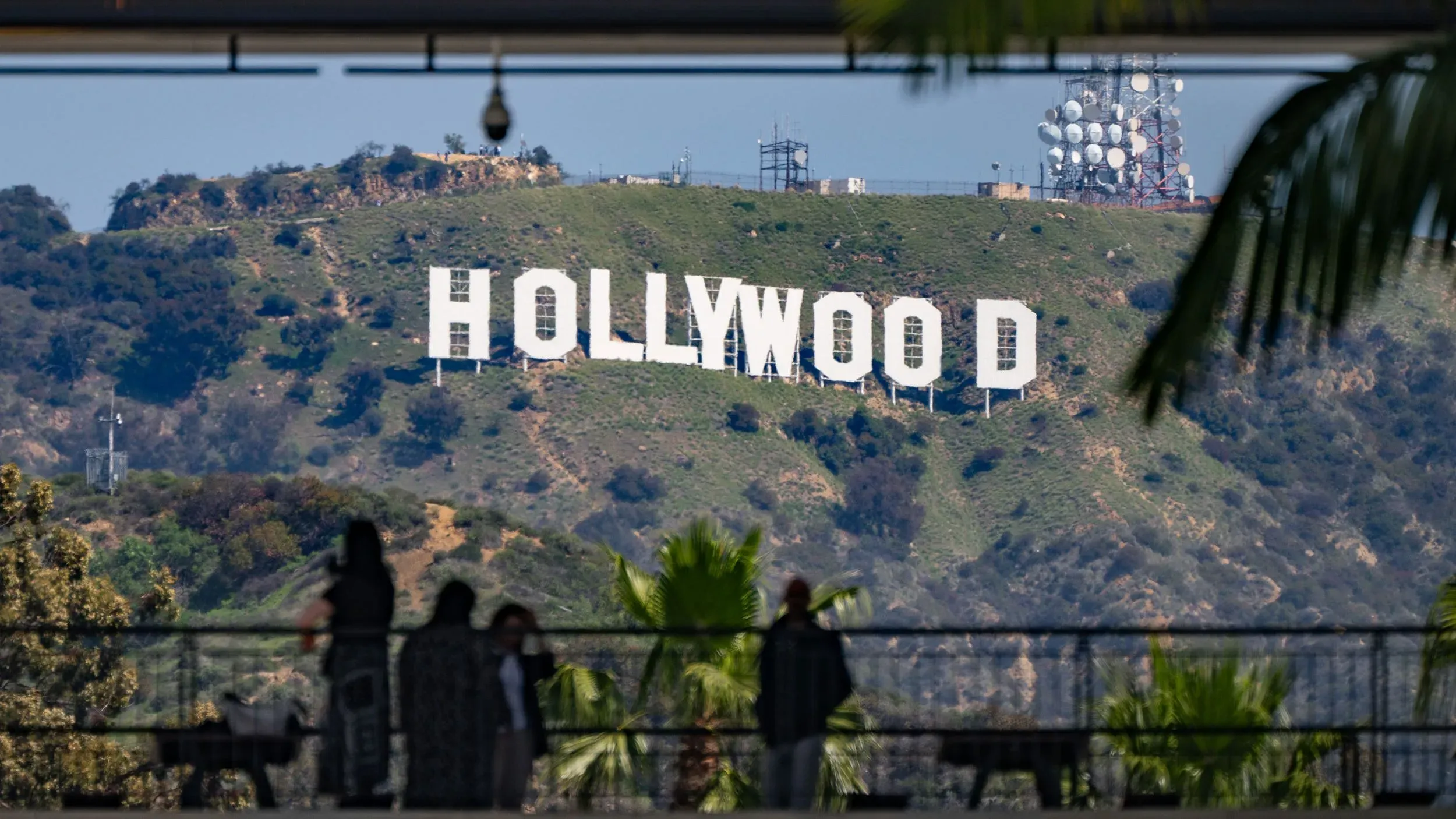 علامة هوليوود الشهيرة تظهر على تل، مع أشخاص يتجولون في المقدمة، تعكس الجدل حول التعريفات الجمركية على الأفلام الأجنبية.