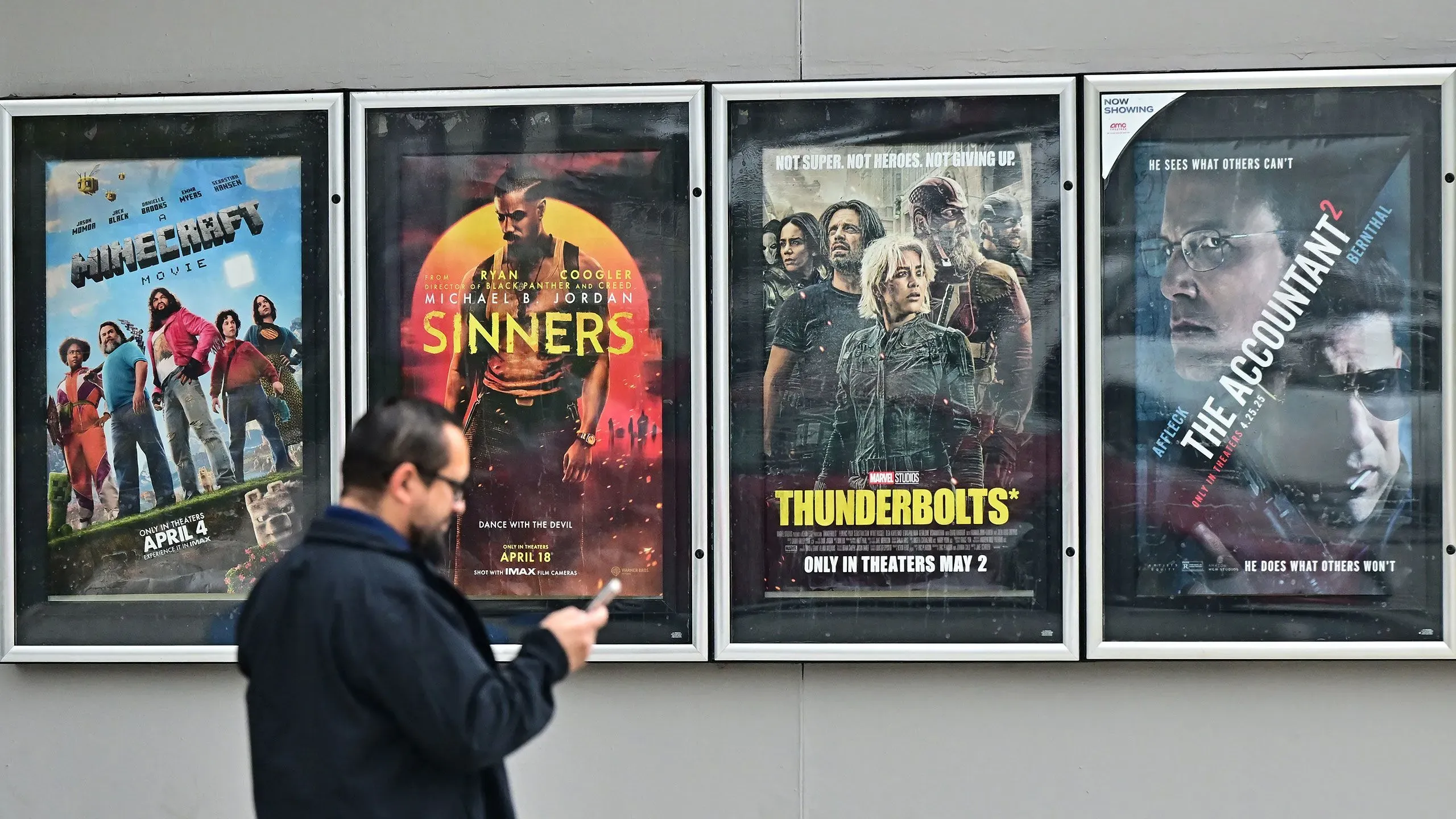 إعلانات أفلام جديدة في دور السينما، تشمل "Minecraft Movie" و"Sinners" و"Thunderbolts" و"The Accountant 2"، بينما يمر رجل بجوارها.