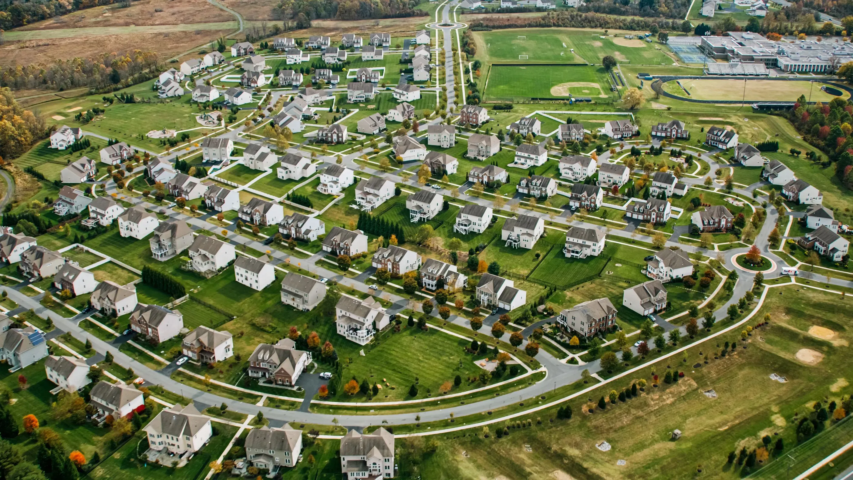 تظهر الصورة منظرًا جويًا لحي سكني يتضمن منازل متعددة محاطة بمساحات خضراء وشوارع متعرجة، مما يعكس التغيرات في سوق الإسكان.