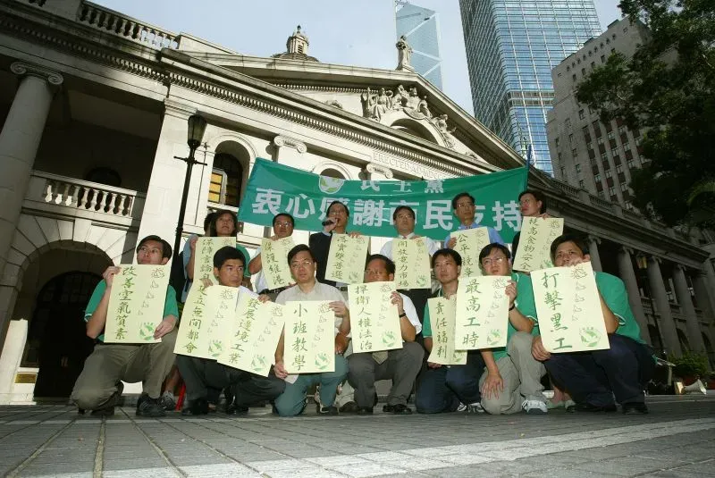 محتجون يحملون لافتات في هونغ كونغ أمام مبنى تاريخي، يعبرون عن دعمهم للديمقراطية في ظل القمع المستمر من بكين.