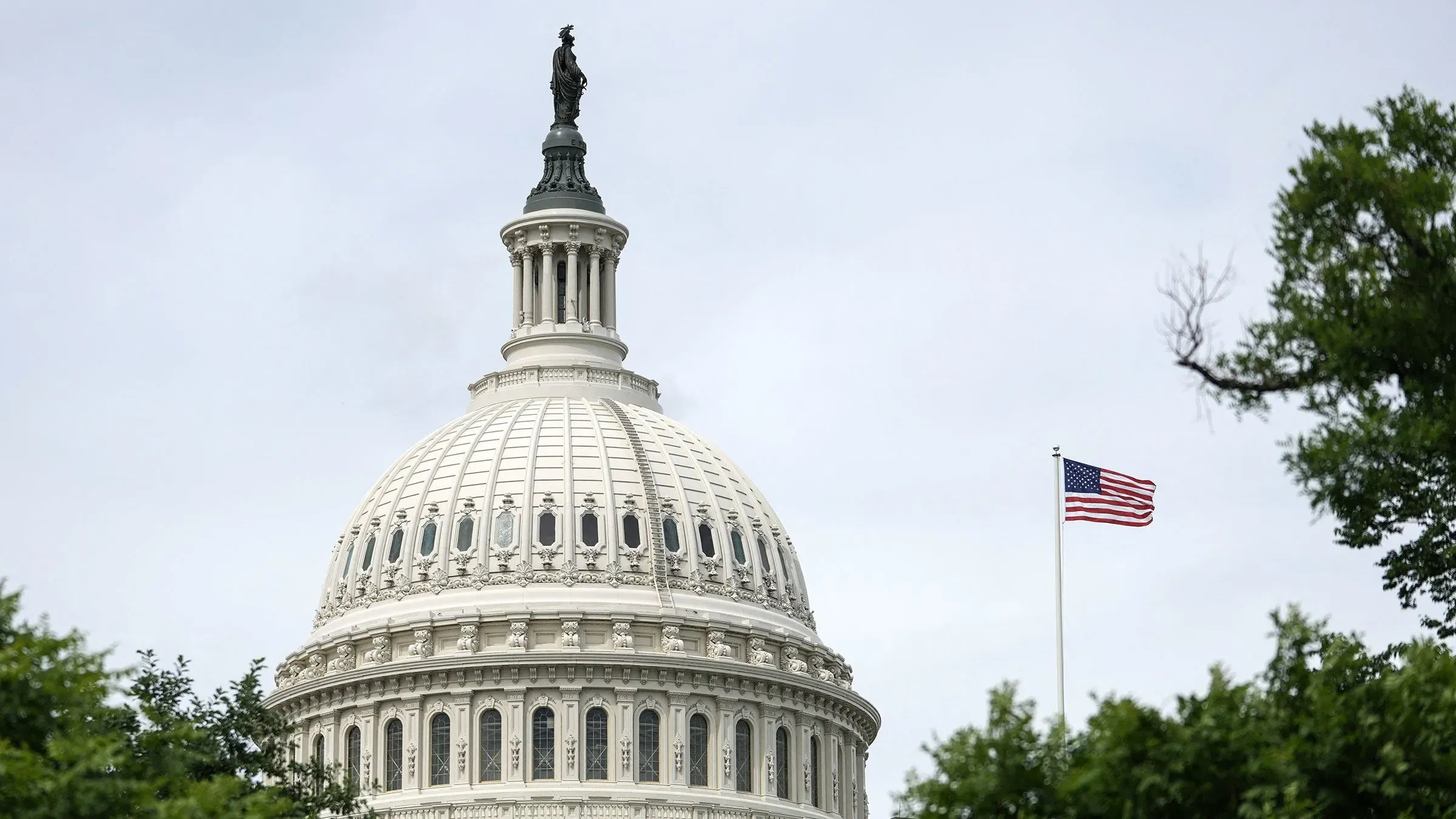 قبة مبنى الكابيتول الأمريكي تبرز تحت سماء غائمة، مع العلم الأمريكي يرفرف بجانبها، مما يعكس أجواء النقاشات السياسية حول مشروع قانون ترامب.