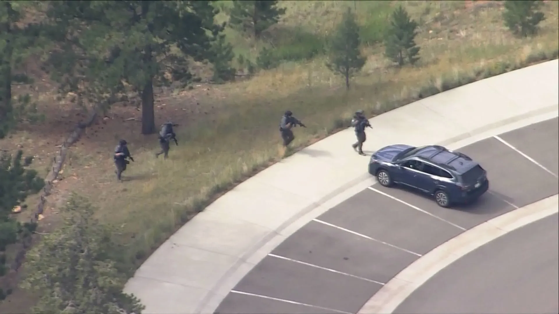 عناصر من قوات إنفاذ القانون يتقدمون عبر منطقة مشجرة قرب موقف سيارات، أثناء البحث عن مشتبه به في متنزه ستاونتون ستيت بكولورادو.