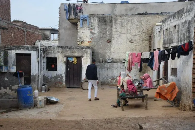 فناء منزل محمد محسن في ميروت، الهند، يظهر جدرانًا متقشرة وأثاثًا قديمًا، حيث يجلس أفراد العائلة معًا وسط ملابس معلقة.