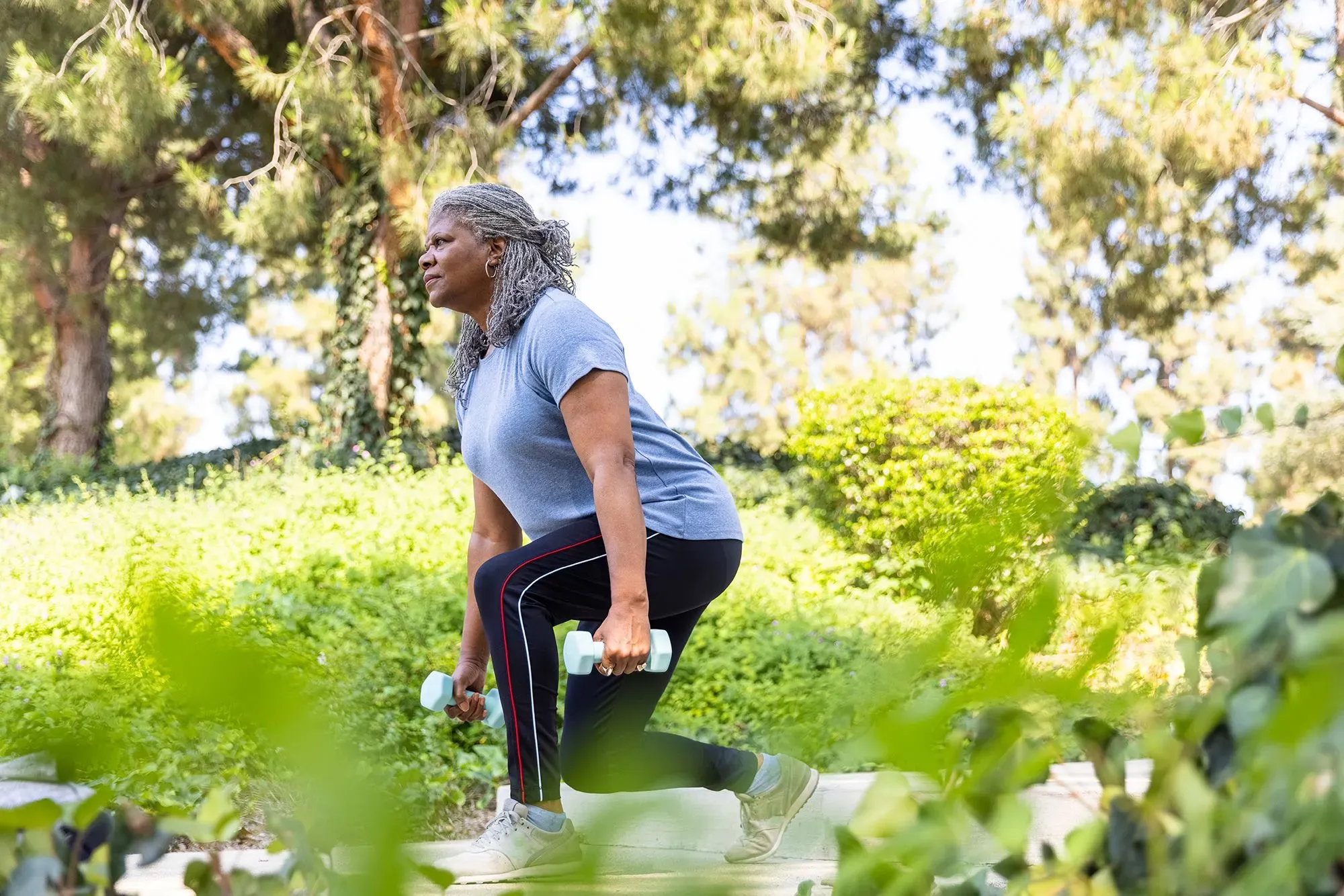 امرأة تمارس تمارين رفع الأثقال في حديقة، تعبر عن أهمية النشاط البدني لصحة العظام، خاصة في سياق هشاشة العظام.