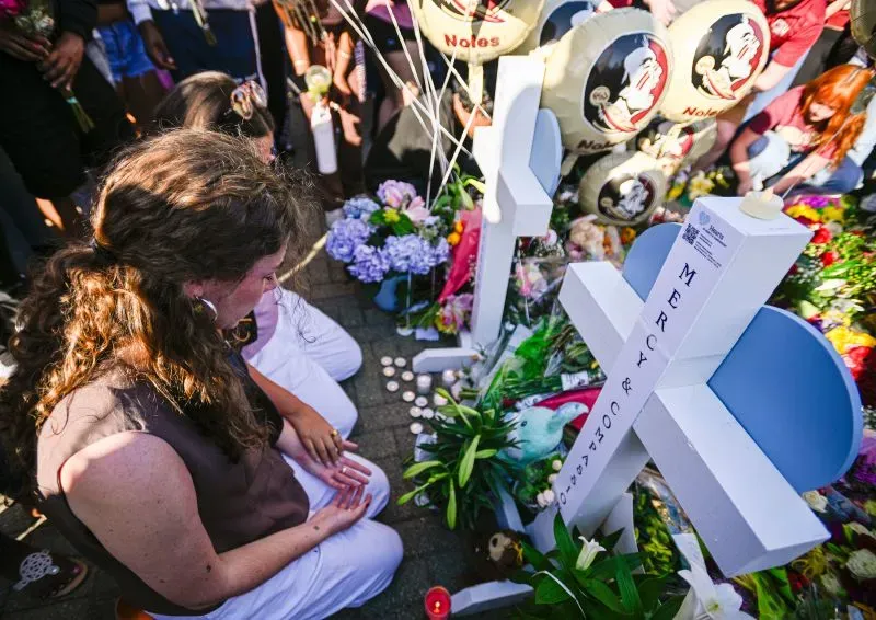 طلاب جامعة ولاية فلوريدا يشاركون في تأبين بعد حادث إطلاق نار، مع زهور وصليب يحمل أسماء الضحايا، مع تعبيرات الحزن والألم.