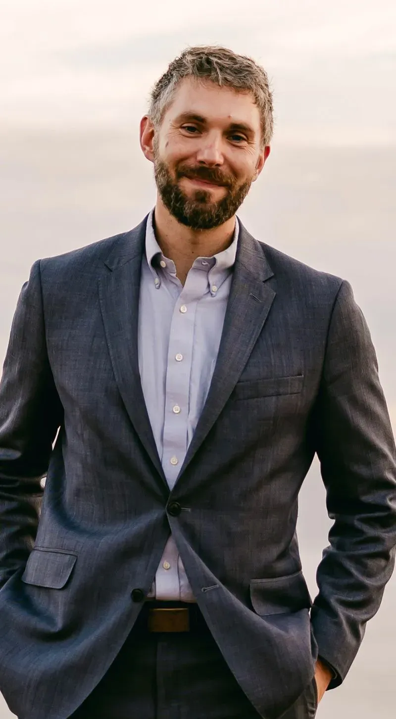 رجل يرتدي بدلة رمادية وقميص أزرق، مبتسمًا في صورة التقطت في بيئة خارجية، تعكس أهمية الوصول إلى الإنترنت في المكتبات.