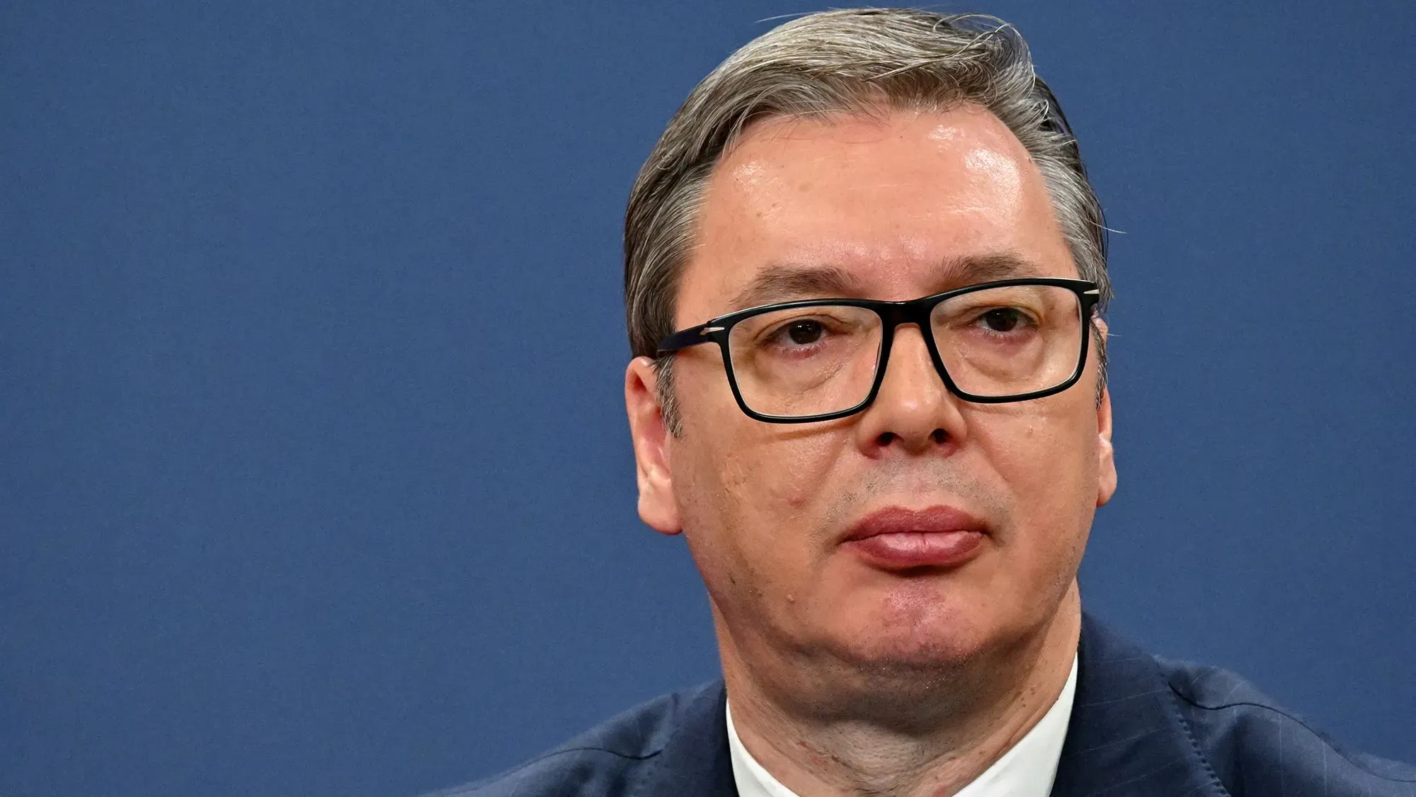 الرئيس الصربي ألكسندر فوسيتش، وهو يرتدي نظارات، يظهر في مؤتمر صحفي. تعكس تعابيره التوتر السياسي في البلاد.