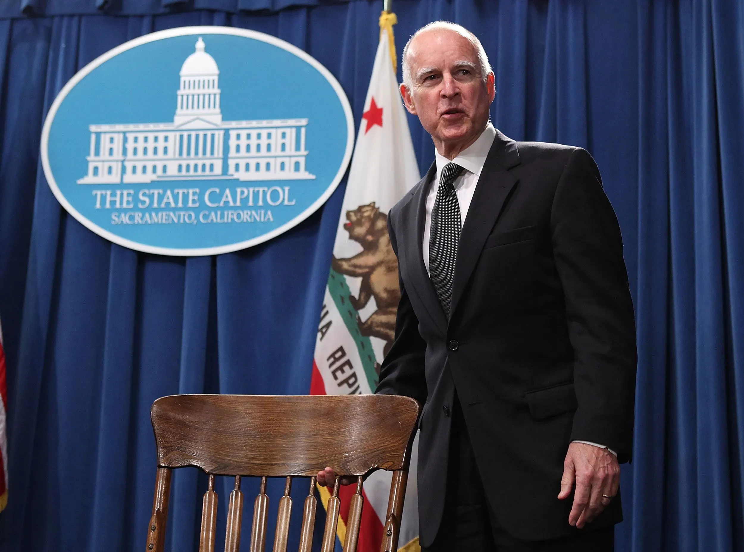 حاكم كاليفورنيا غافين نيوسوم يقف أمام منصة تحمل شعار الولاية، مستعدًا لمناقشة قرارات الإفراج المشروط للأخوين مينينديز.