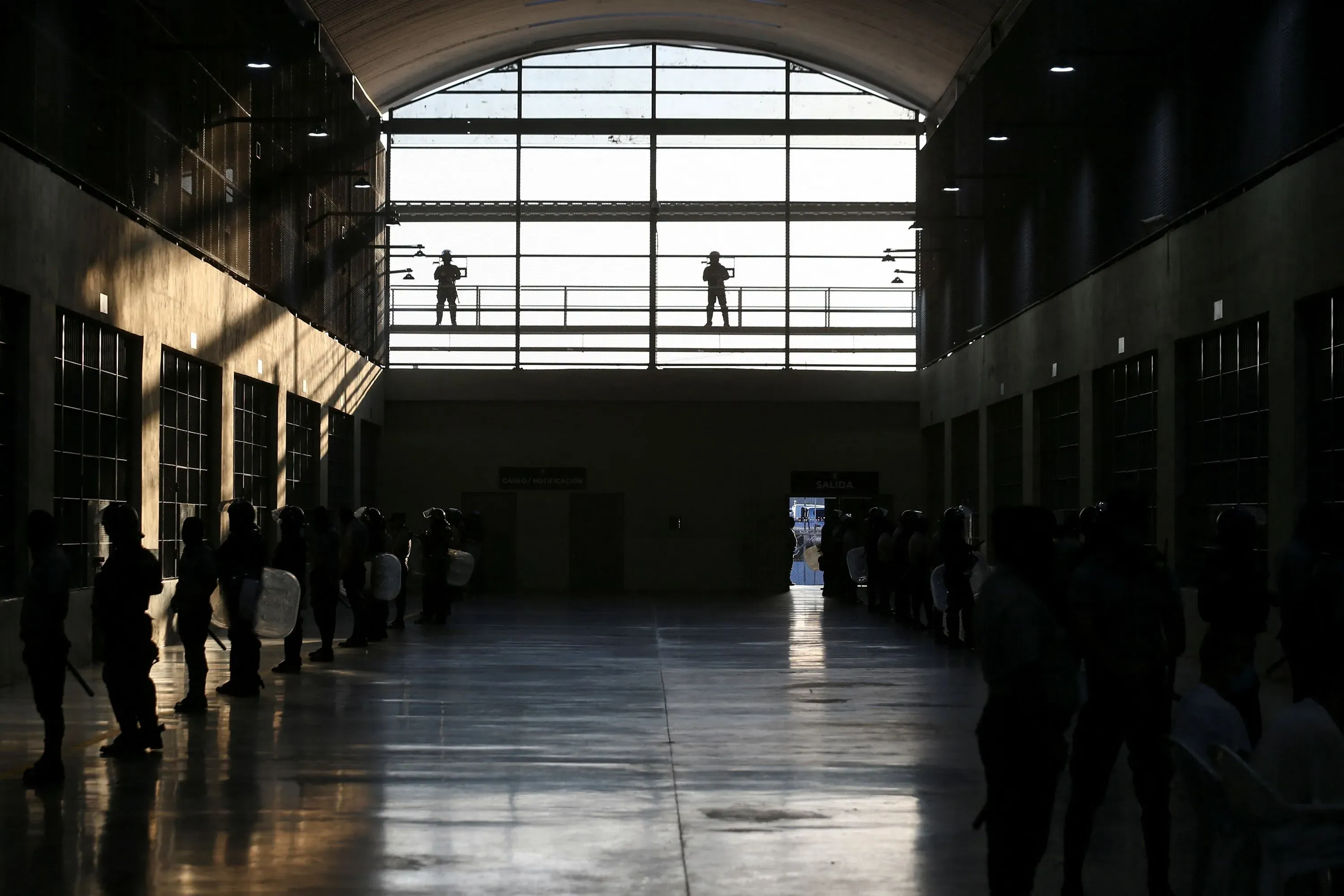 صورة لمركز احتجاز في السلفادور، حيث يقف حراس مسلحون فوق منصة بينما يتجمع المحتجزون في صفوف أسفل المبنى.