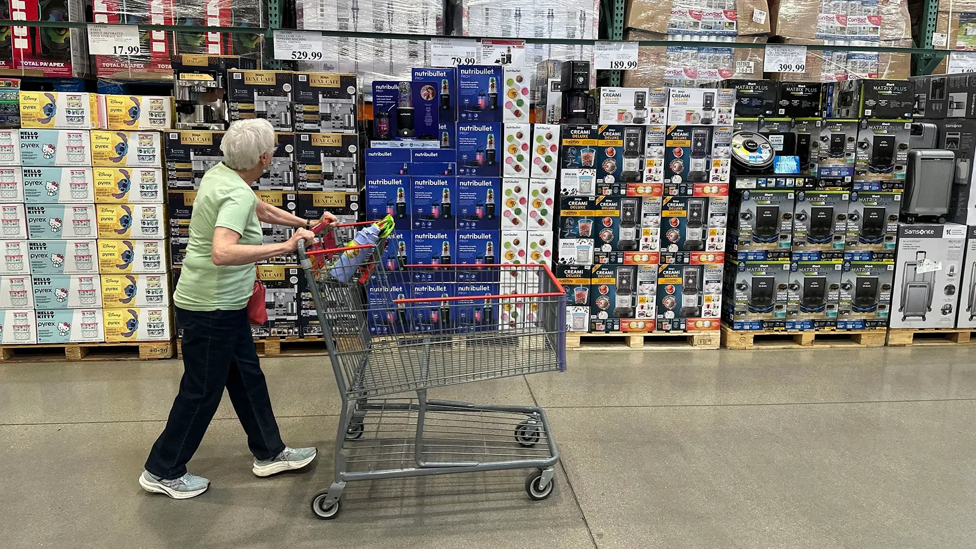 امرأة مسنّة تتسوق في متجر كبير، محاطة بأرفف مليئة بالمنتجات الكهربائية والبقالة، تعكس تأثير التضخم على الإنفاق.