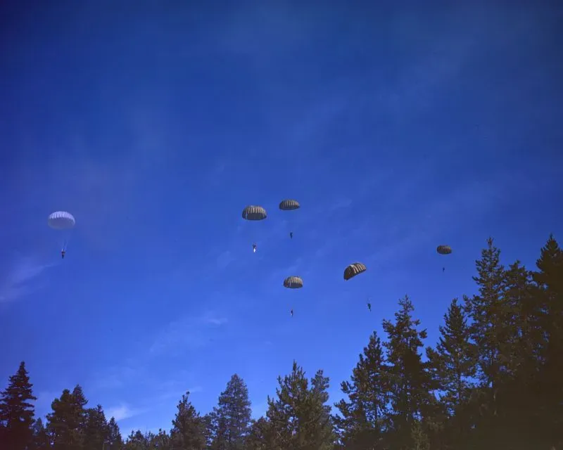 مجموعة من المظليين أثناء القفز بالمظلات فوق غابة، في سياق تاريخي يتعلق بمهمة إخماد حرائق الغابات خلال الحرب العالمية الثانية.