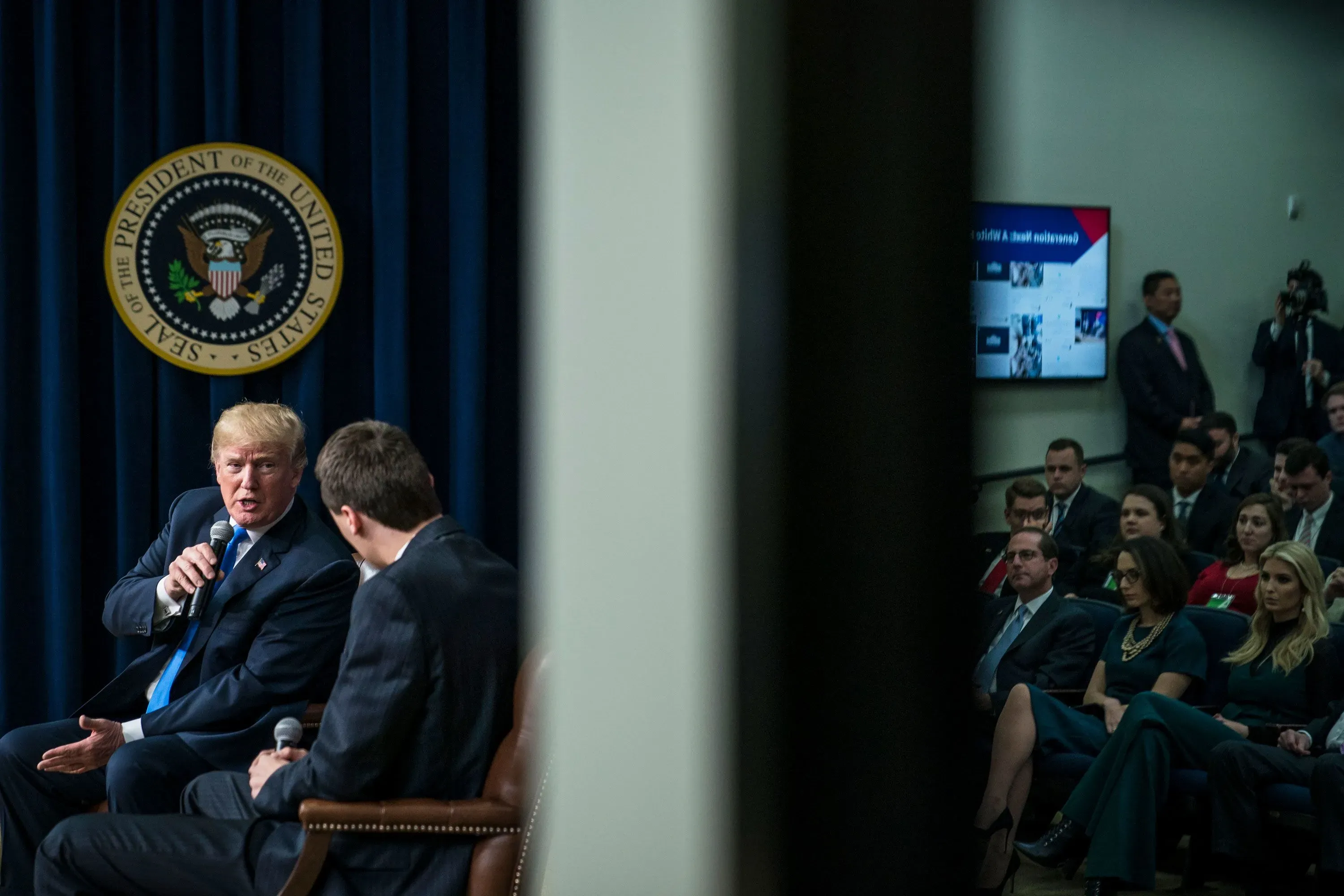 تشارلي كيرك يتحدث مع الرئيس ترامب خلال حدث في البيت الأبيض، مع وجود جمهور من الحضور خلفهم.