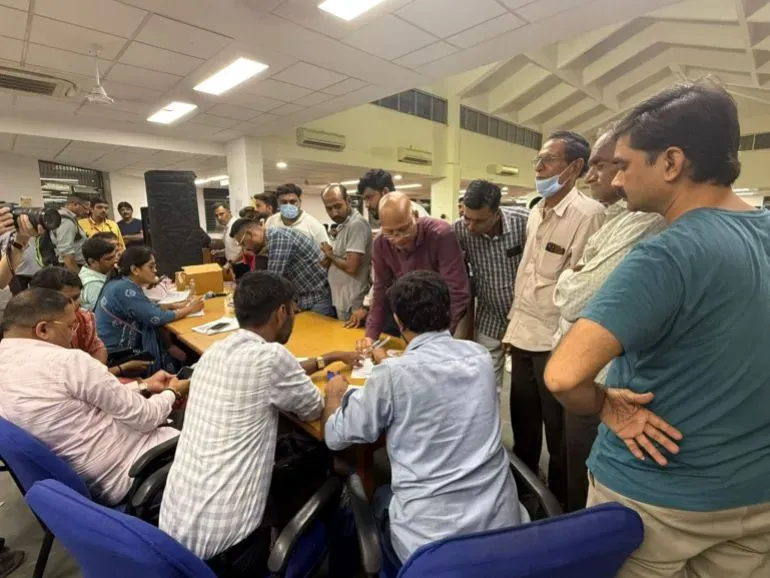 حشود من الناس تتجمع حول طاولة في مركز طوارئ بعد تحطم الطائرة، حيث يتبادلون المعلومات حول الحادث المأساوي.