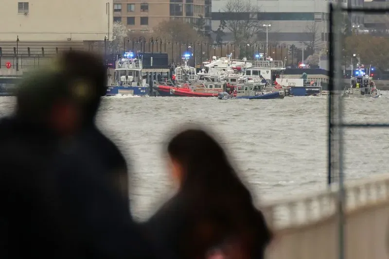 استجابة طوارئ في نهر هدسون بعد حادث مروحية، مع ظهور قوارب الإنقاذ في الخلفية وأشخاص يتابعون المشهد من الشاطئ.