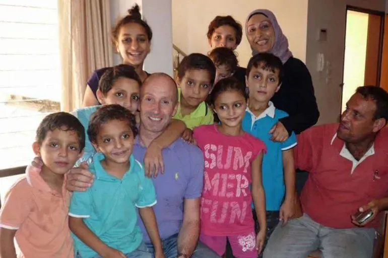 مجموعة من الأطفال والبالغين يجلسون معًا في غرفة، مبتسمين ويظهرون روح العائلة والتواصل، مما يعكس ذكريات الطفولة في غزة.