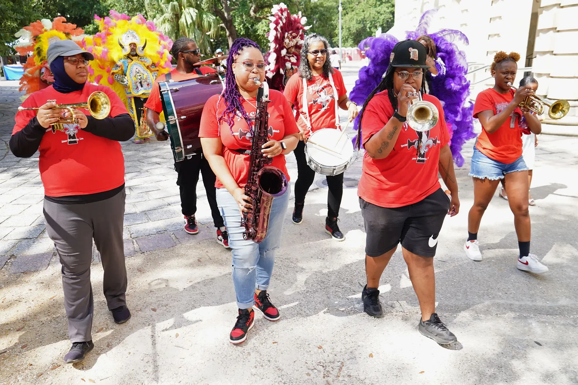 فرقة موسيقية نحاسية تسير في شوارع نيو أورلينز، يرتدي أعضاؤها قمصان حمراء، وتظهر أجواء احتفالية تعكس ثقافة المدينة الغنية.