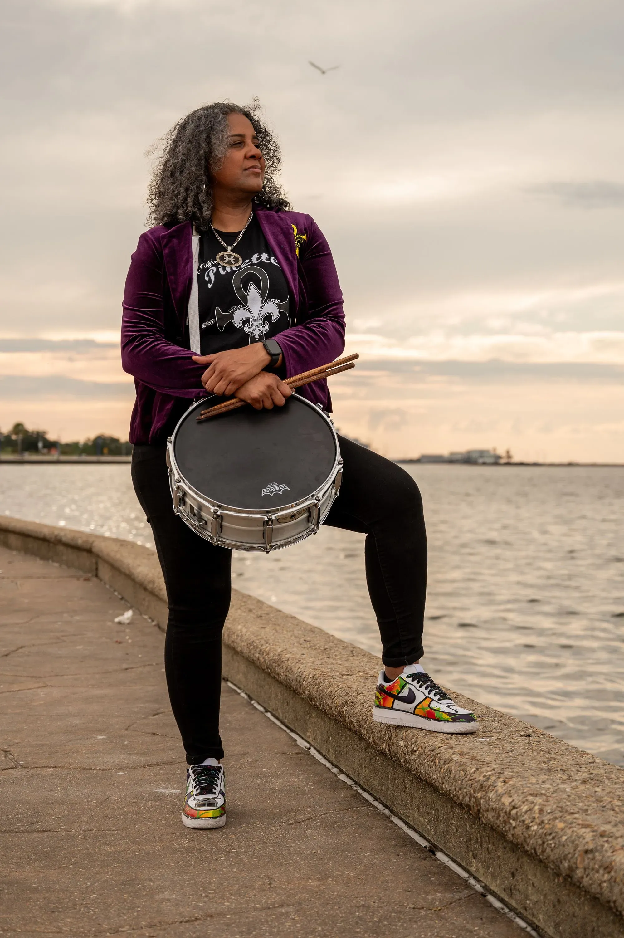 امرأة تحمل طبلًا على ضفة نهر في نيو أورلينز، ترتدي ملابس ملونة، تعبر عن روح المدينة الموسيقية وتقاليدها الثقافية.