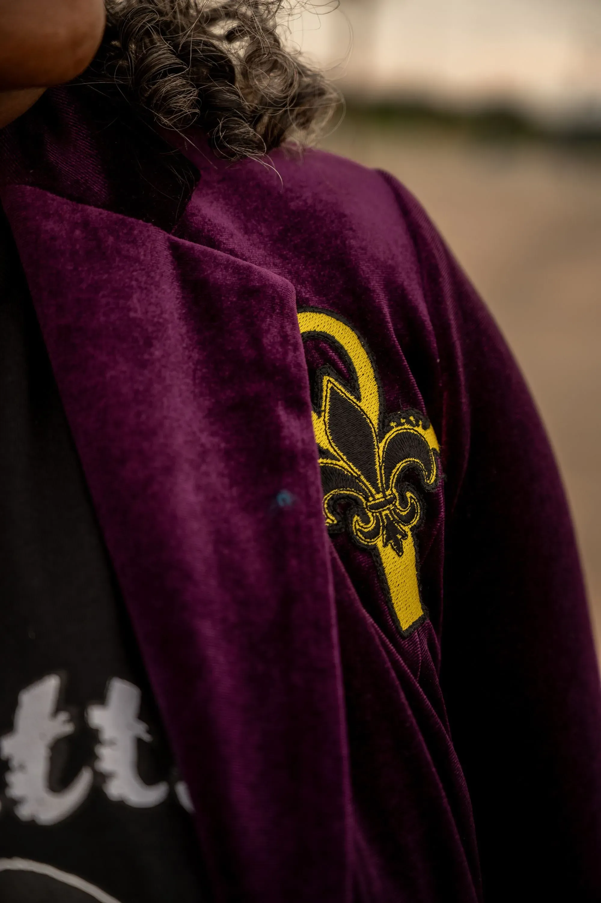 شخص يرتدي سترة بنفسجية مزينة بشعار الزهرة الفرنسية، يعكس تراث نيو أورلينز الثقافي والموسيقي.