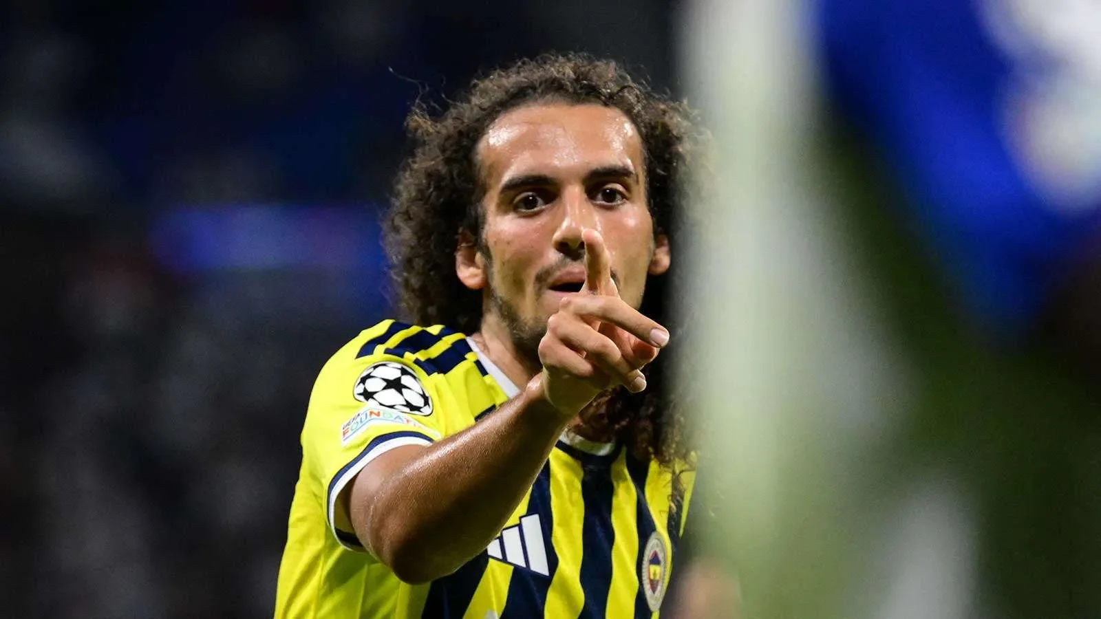 لاعب كرة قدم من فريق فنربخشة التركي يرتدي قميص أصفر وأزرق يحتفل بإشارة يد خلال مباراة دوري أبطال أوروبا.