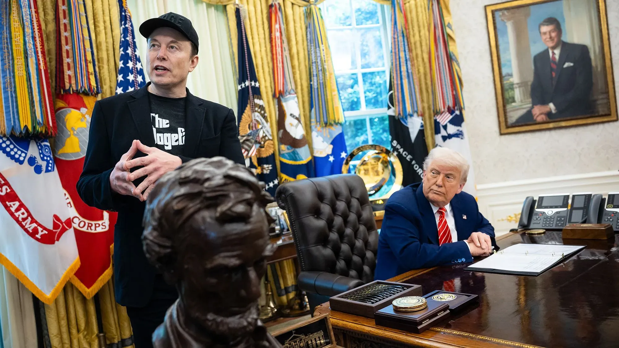 إيلون ماسك يتحدث في المكتب البيضاوي بينما يستمع له دونالد ترامب، مع وجود تمثال لنابليون في المقدمة.
