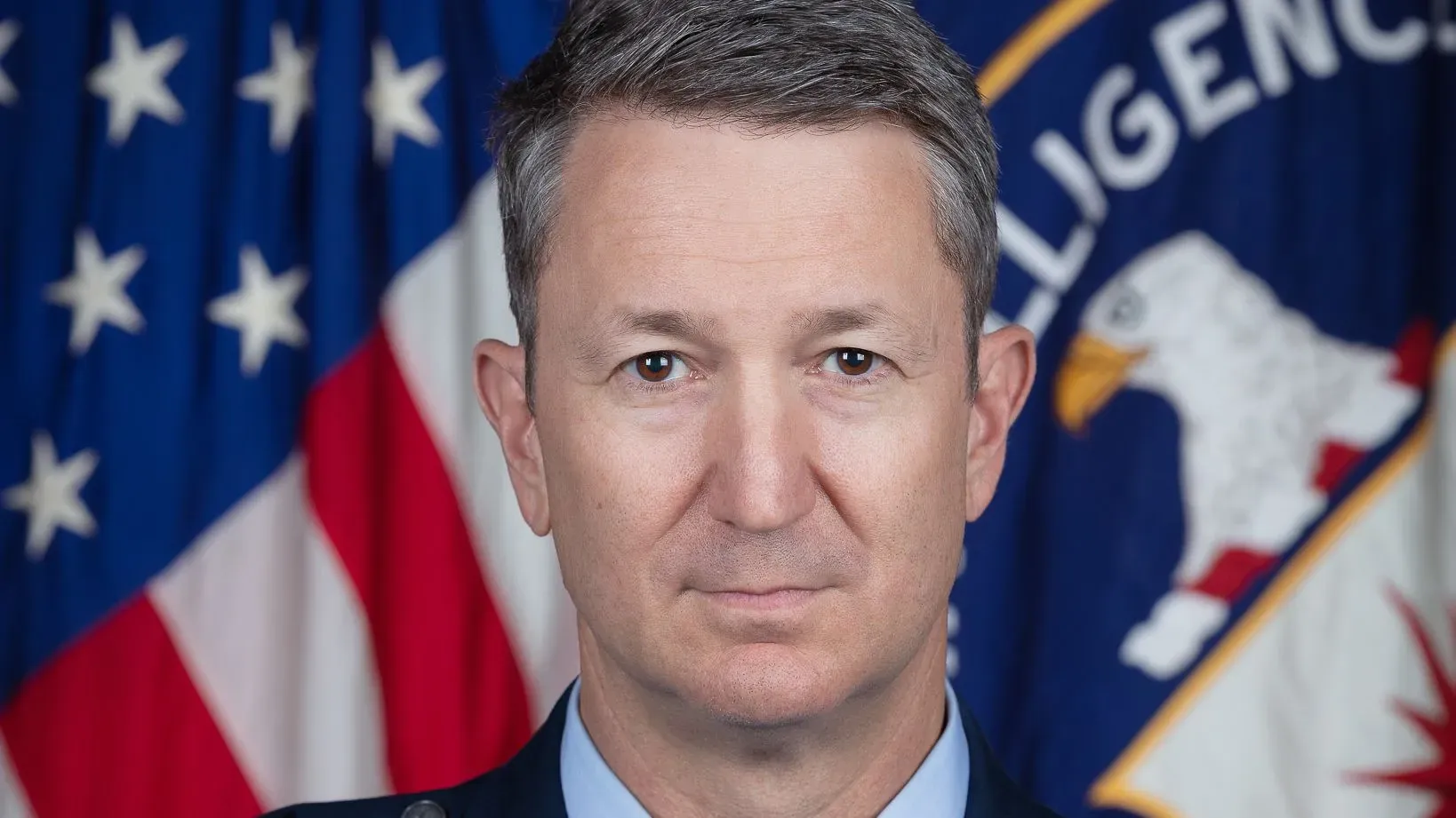 الجنرال المتقاعد جون كاين، طيار محترف في سلاح الجو الأمريكي، يرتدي زياً رسمياً أمام علم الولايات المتحدة، بعد تعيينه رئيساً لهيئة الأركان المشتركة.