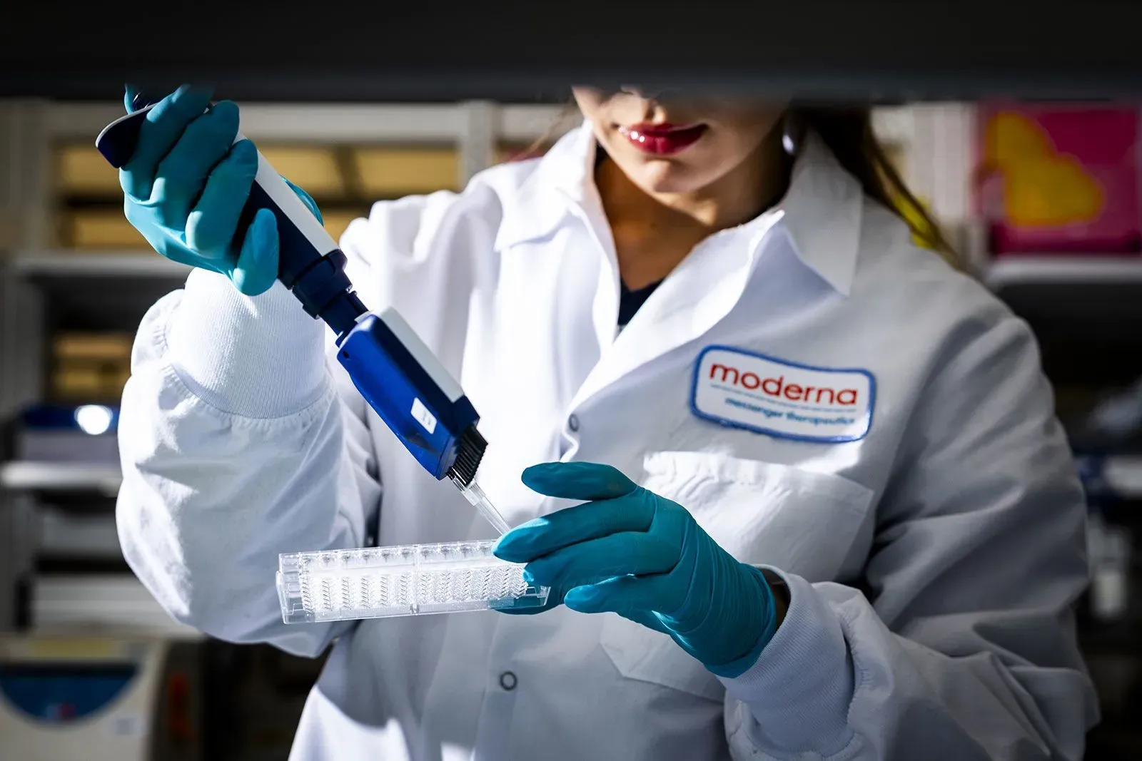 عالمة تعمل في مختبر، تستخدم ماصة لنقل سائل إلى أنابيب اختبار، في سياق أبحاث لقاحات كوفيد-19.