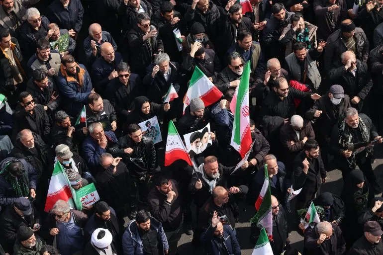 مظاهرة حاشدة في إيران، حيث يحمل المشاركون الأعلام الإيرانية وصوراً لرموز سياسية، تعبيراً عن تأييدهم في سياق التوترات الإقليمية.