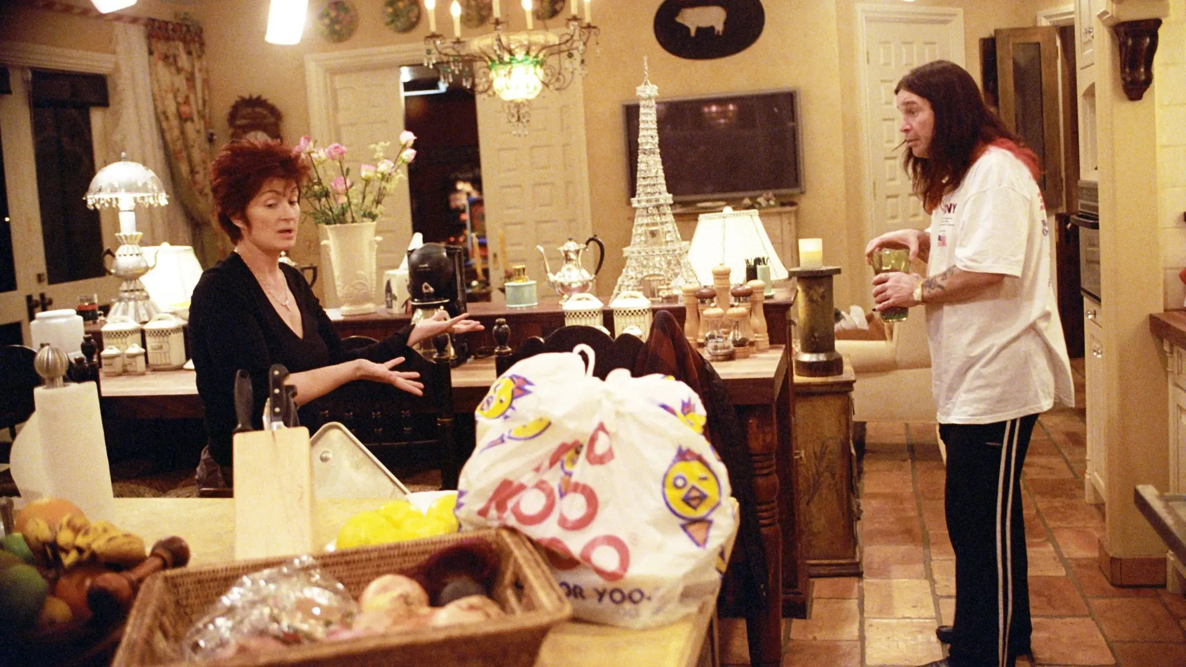 مشهد من برنامج "ذا أوسبورنز" يظهر شارون أوزبورن تتحدث مع أوزي أوزبورن في مطبخ منزلهما، مع تفاصيل منزلية واضحة.