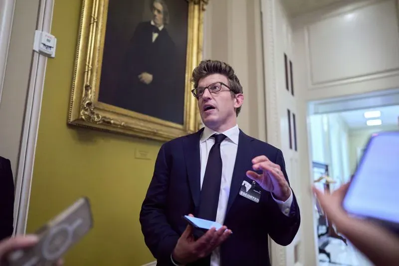 رجل يرتدي بدلة رسمية يتحدث بحماس عن الطاقة المتجددة في ممر بمبنى حكومي، بينما تظهر لوحة تاريخية خلفه.