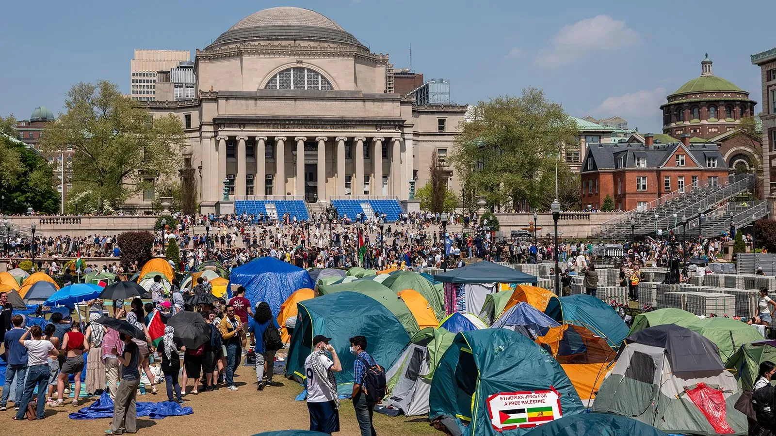 تظهر الصورة تجمعًا كبيرًا للطلاب في حرم جامعة كولومبيا، مع خيام ملونة تعبر عن احتجاجات ضد سياسات الهجرة، حيث يتواجد عدد كبير من المتظاهرين.