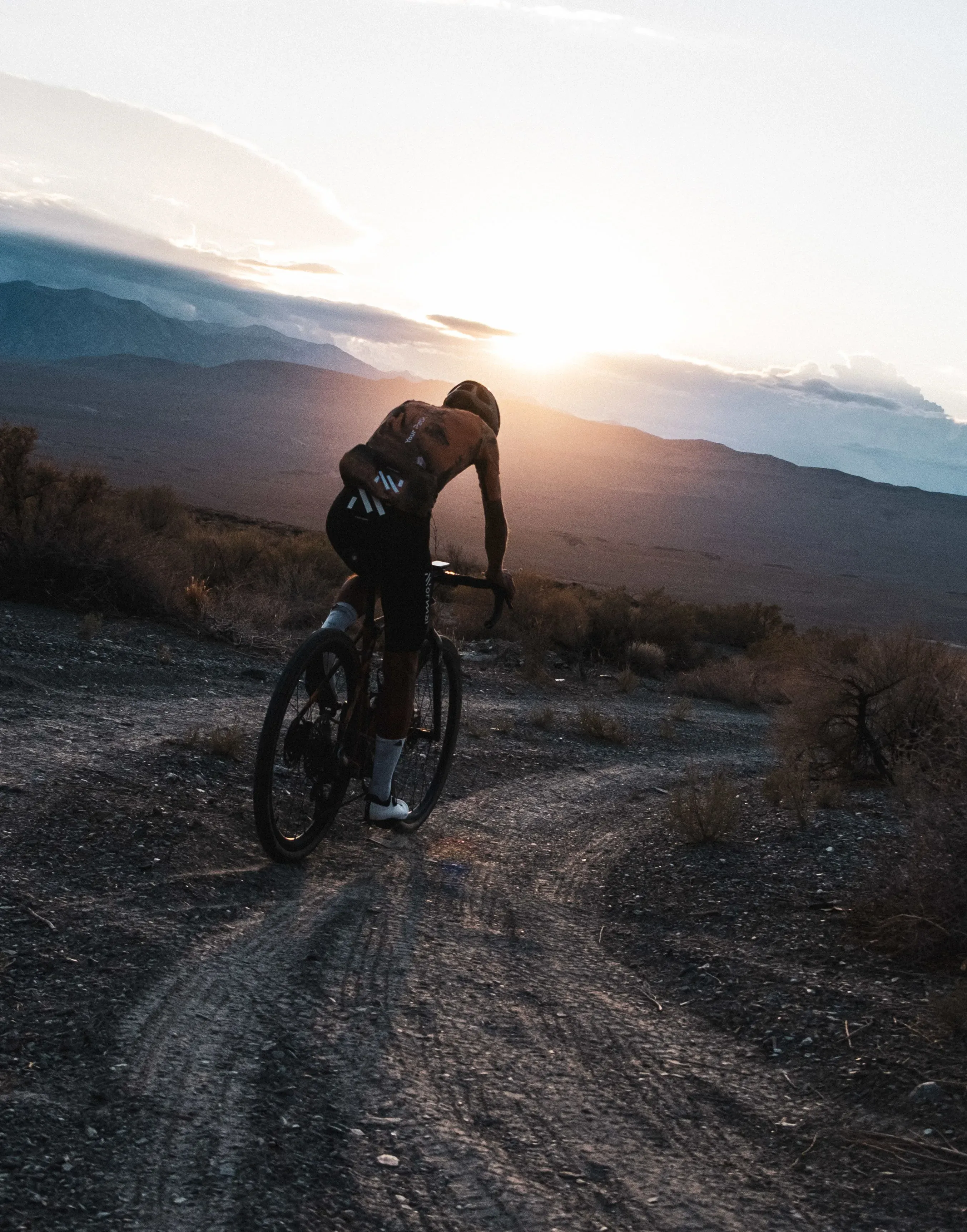 راكب دراجة هوائية في صحراء جبلية عند غروب الشمس، يرتدي ملابس رياضية ويحمل معدات استكشافية، مع خلفية من الجبال والسماء المضيئة.